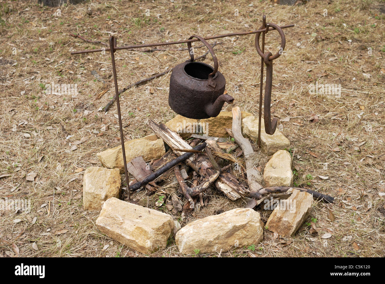 Old rusty kettle on iron frame over an unlit open fire outside in