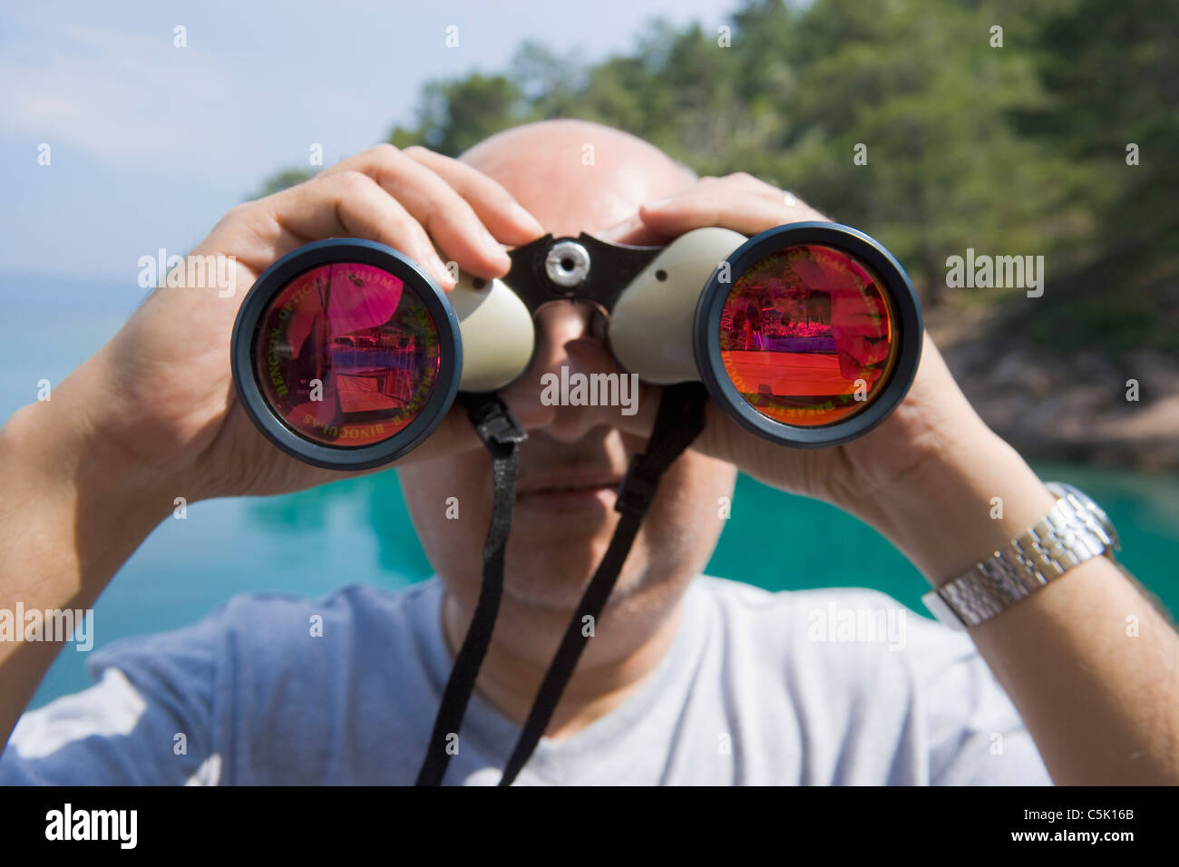 Bald man looking through binoculars with oink glasses, Bodrum, Gokova, Turkey Stock Photo