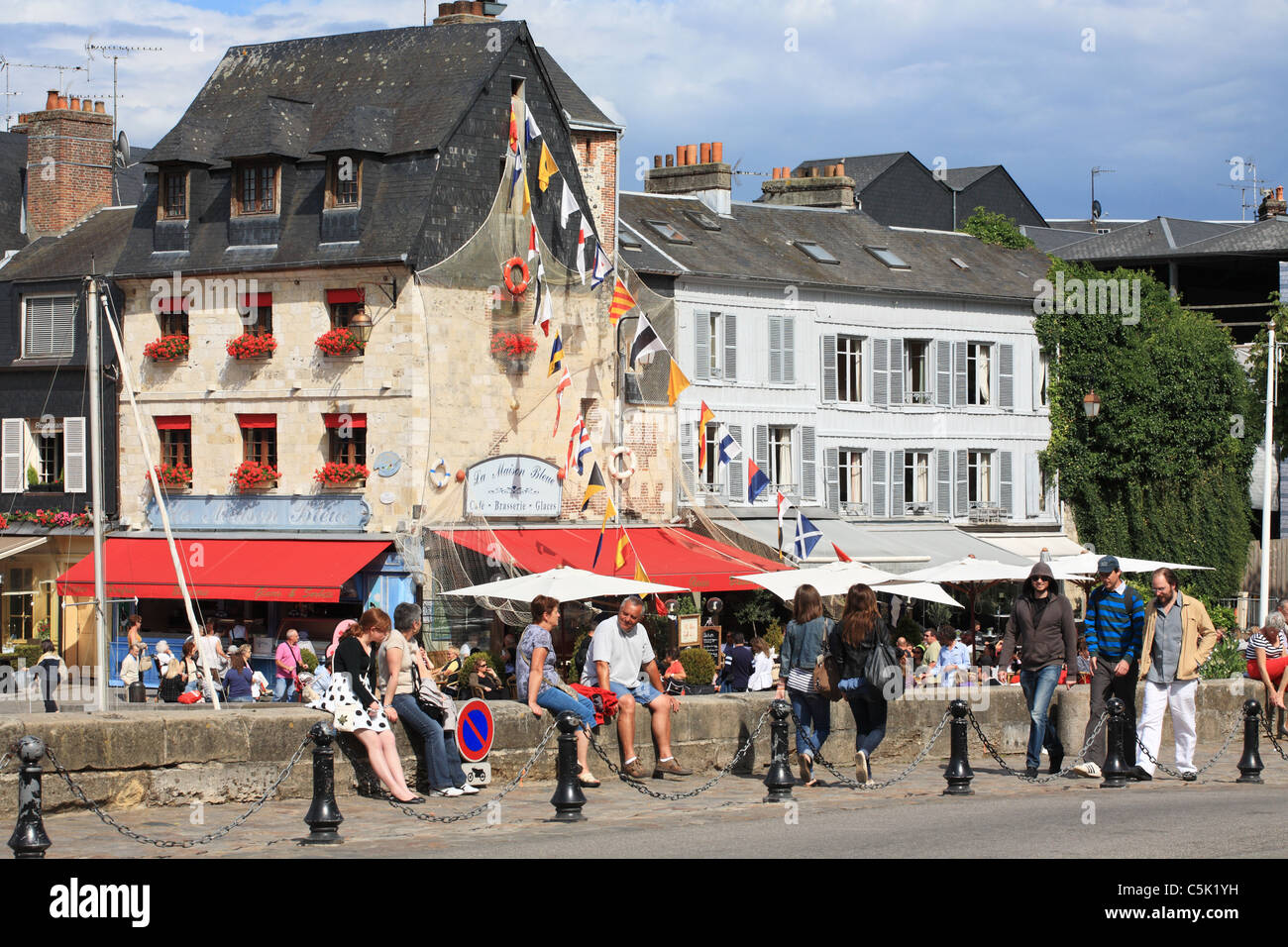 People sitting on the harbour wall at Honfleur outside La Maison Bleue restaurant, Normandy, France Stock Photo
