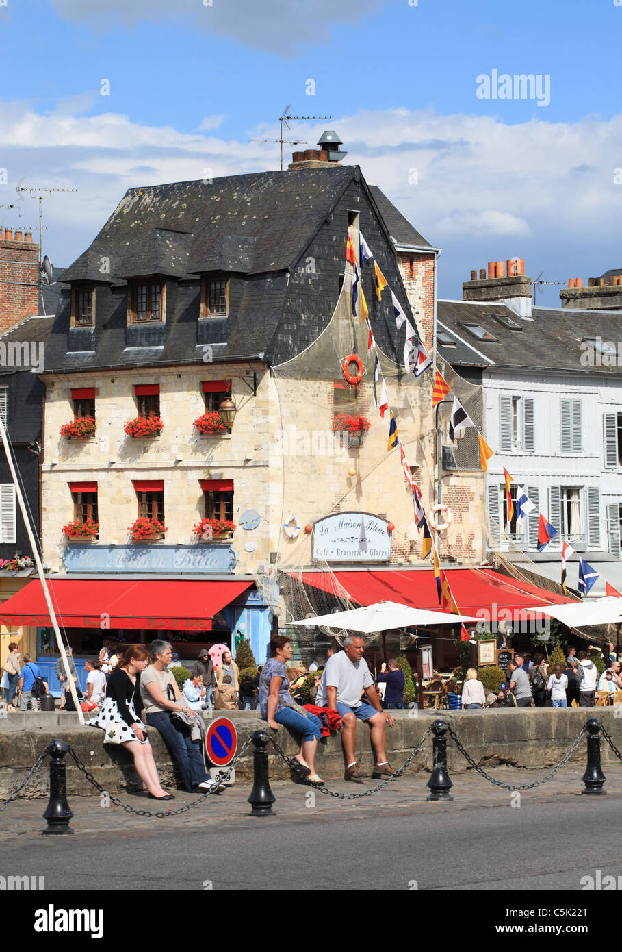 People sitting on the harbour wall at Honfleur outside La Maison Bleue restaurant, Normandy, France Stock Photo