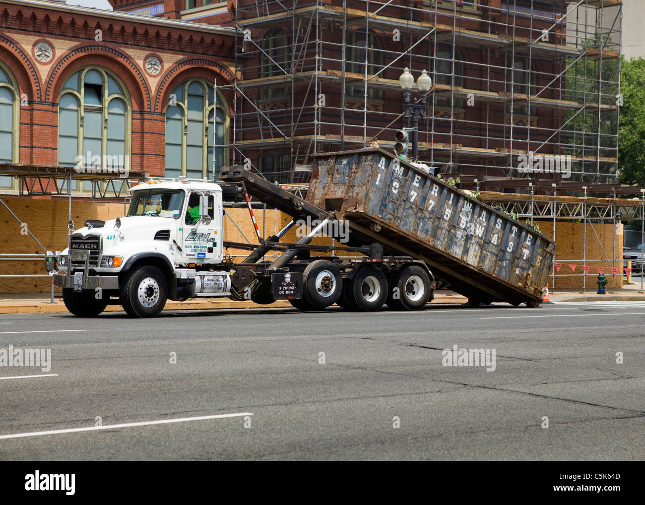A dumpster truck picking up a full container from a construction site Stock Photo