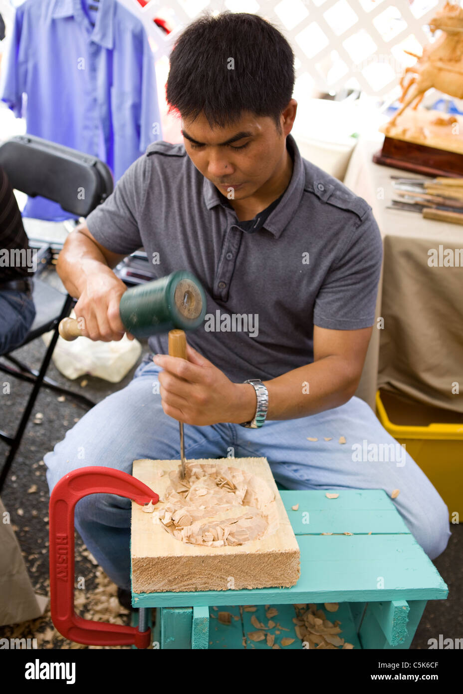 A Filipino man carving a piece of wood using chisel and rubber mallet