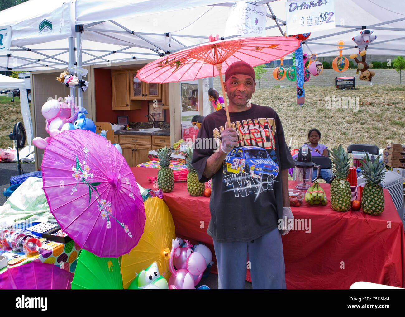 An outdoor festival gift stall salesman holds up an Asian summer umbrella Stock Photo