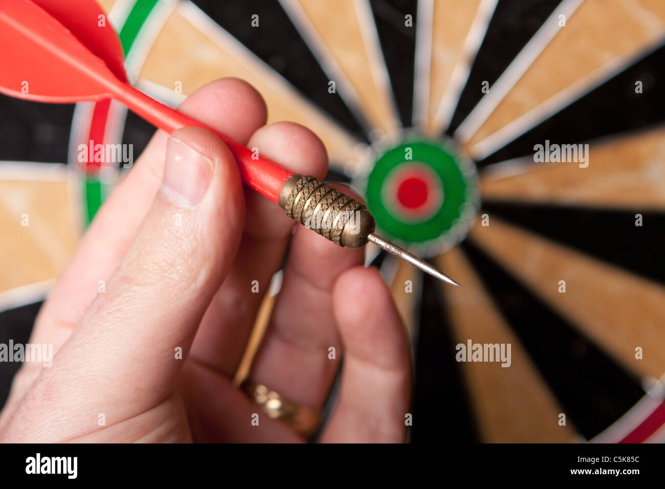 A hand holding a dart getting ready to aim at the dartboard. Shallow depth of field. Stock Photo