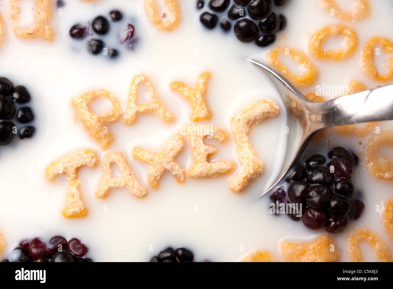The words PAY TAXES spelled out of letter shaped cereal pieces floating in a milk filled cereal bowl. Stock Photo
