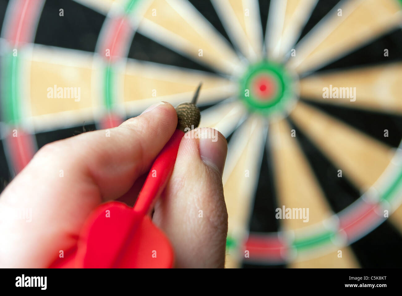 A hand holding a dart getting ready to aim at the dartboard. Shallow depth of field. Stock Photo