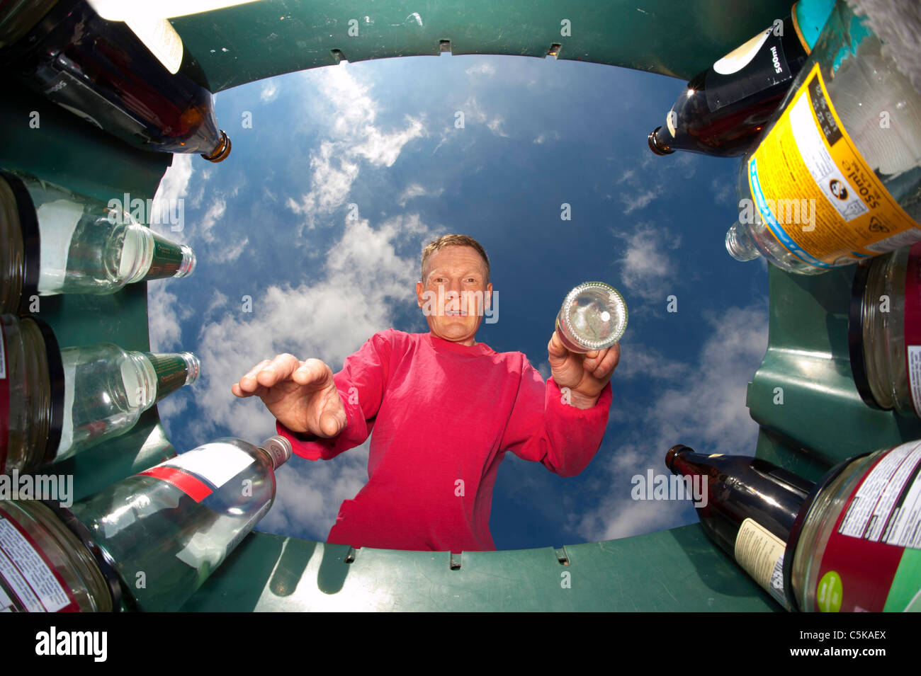 man throwing glass bottle into green recycling bin for recycling Stock Photo