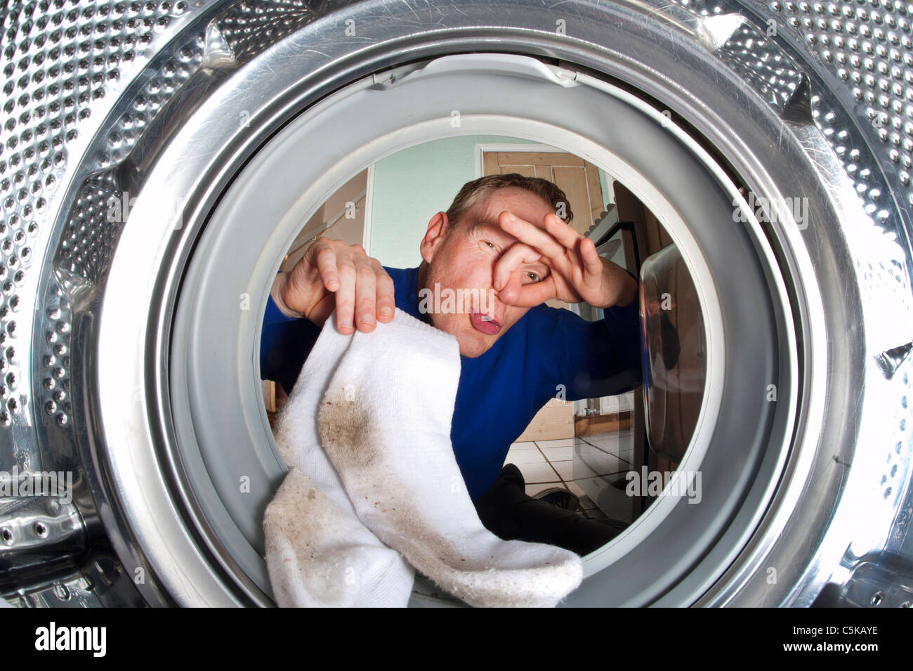 man holding nose putting smelly dirty socks into washing machine Stock Photo