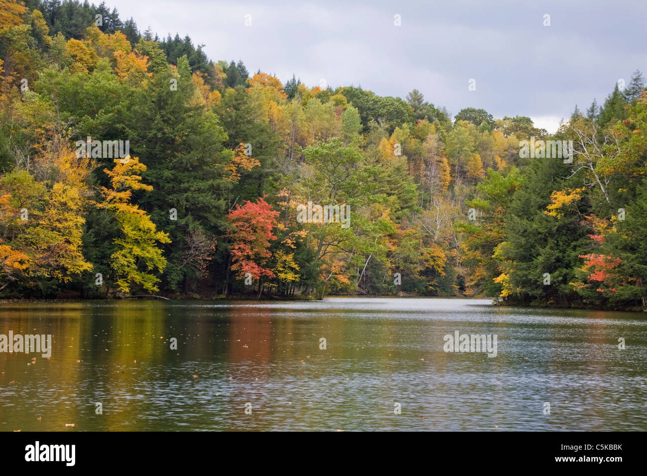 Emerald lake surrounded by mountainsides of trees in Fall color. Stock Photo
