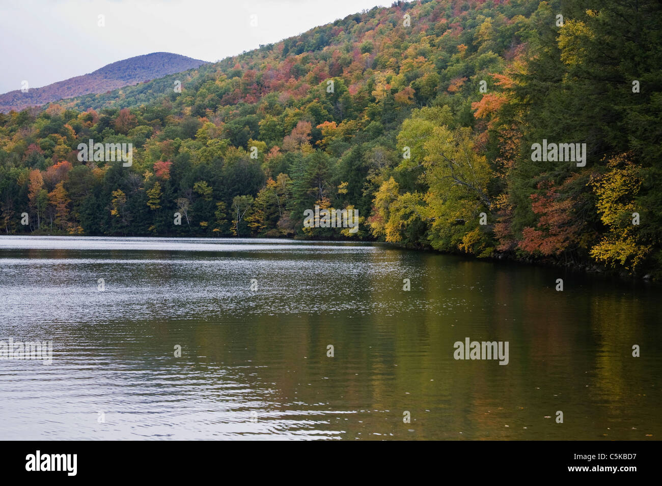 Emerald lake surrounded by mountainsides of trees in Fall color. Stock Photo