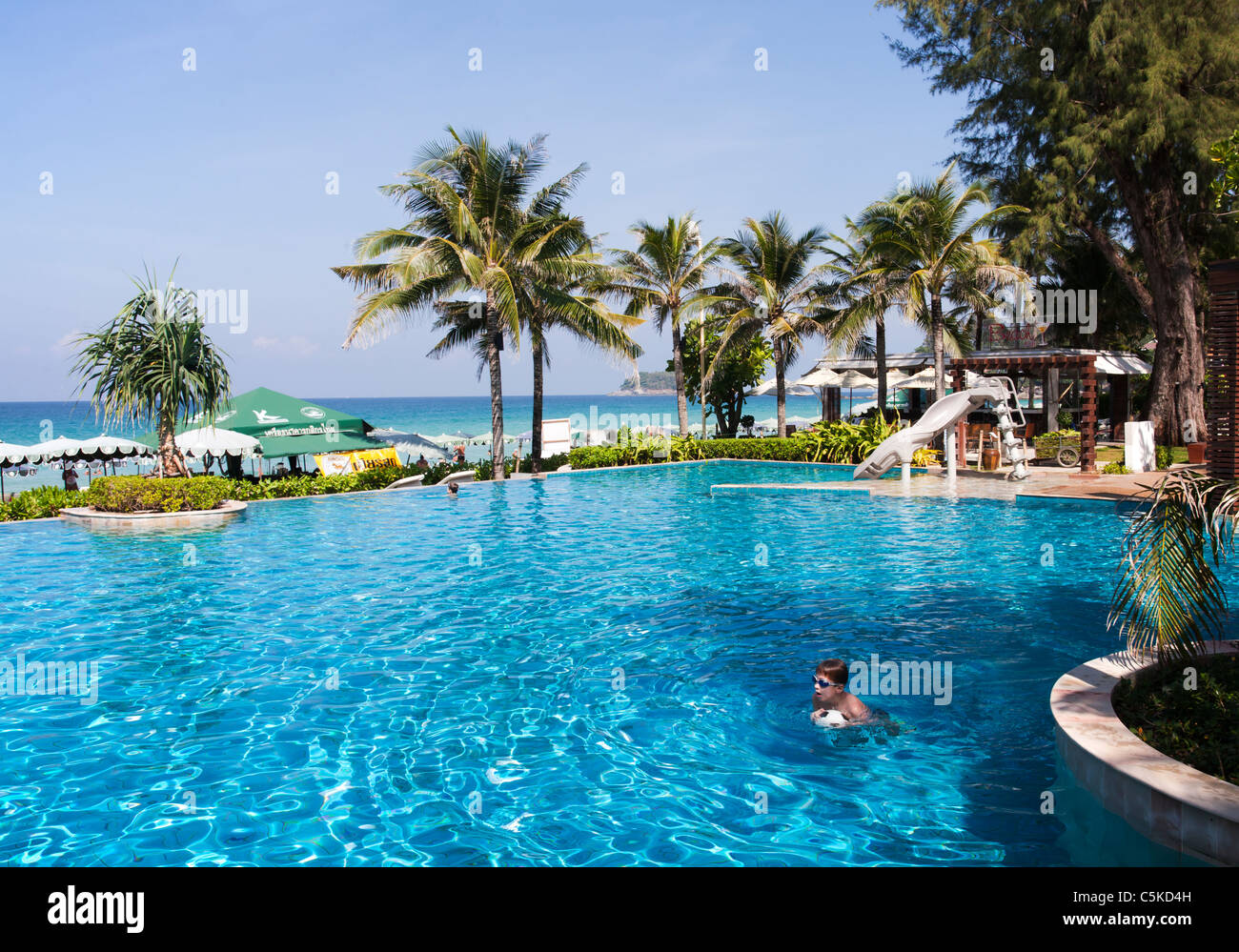 Tropical Hotel swimming pool with swimming child and view towards blue Andaman Sea Stock Photo