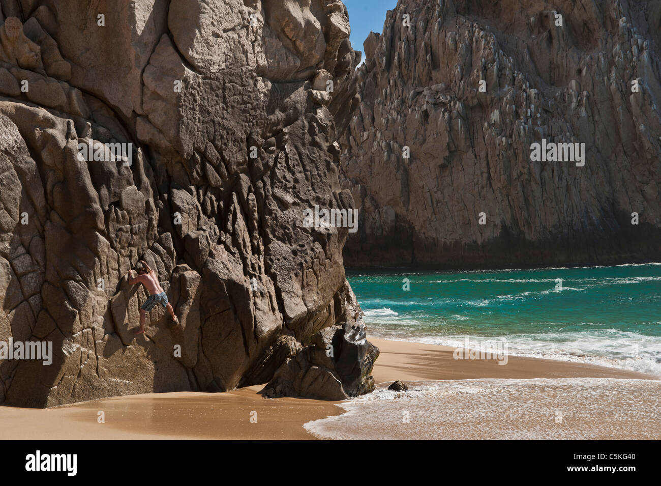 Man crawling along on a huge rock wall near Pacific ocean. Stock Photo