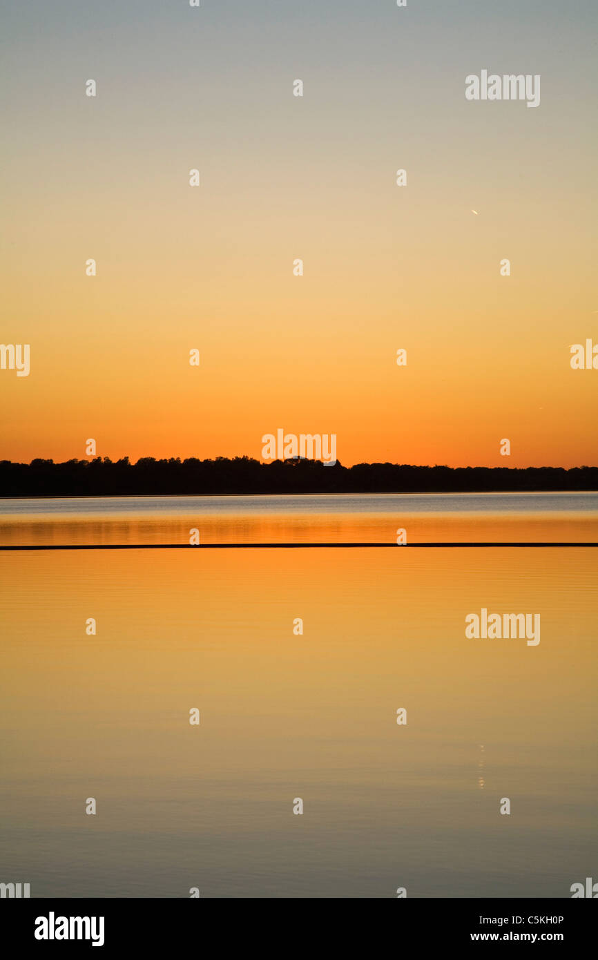 Orange sunset reflected on calm lake water. Stock Photo