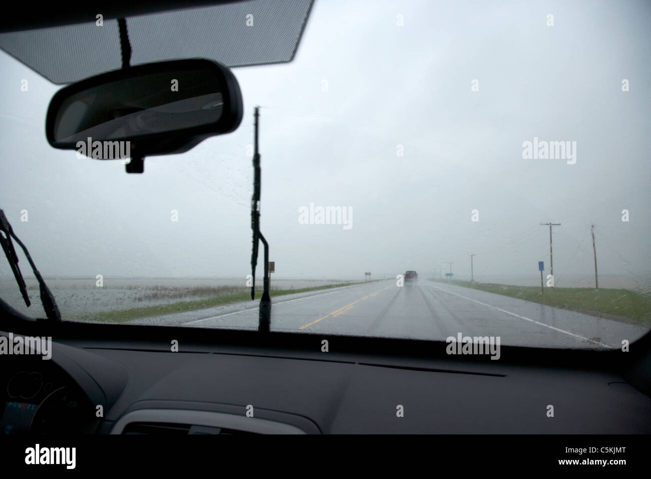 car driving on single highway through heavy rainstorm and flooding fields in southern saskatchewan canada Stock Photo