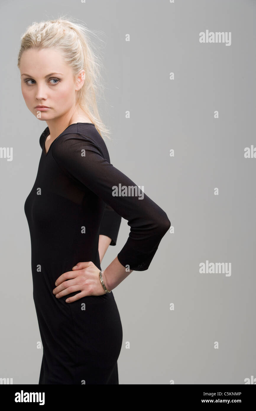 A young blonde woman (22) wearing a black dress, grey background Stock Photo