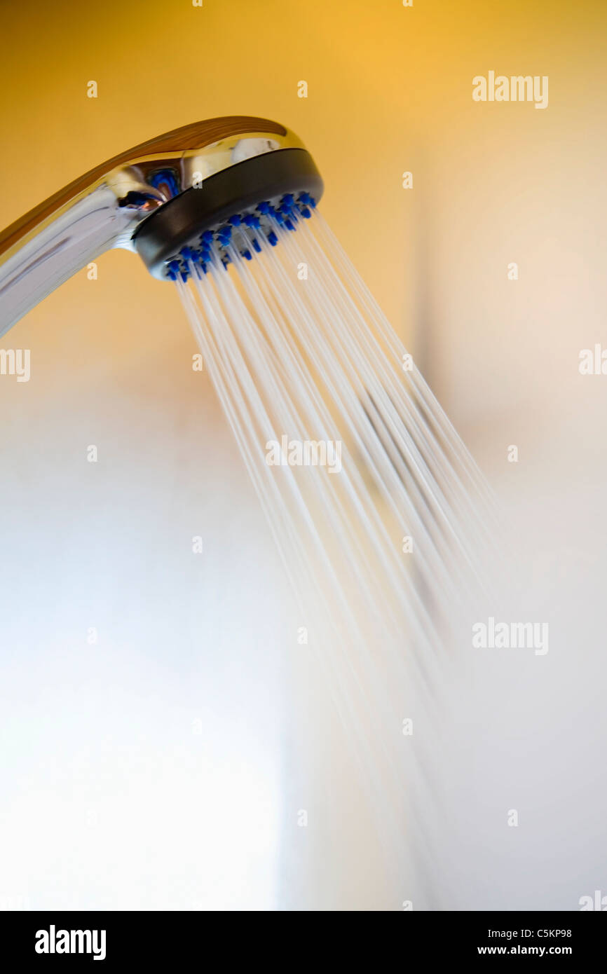 Shower head with hot water and steam coming out, yellow wall in background Stock Photo