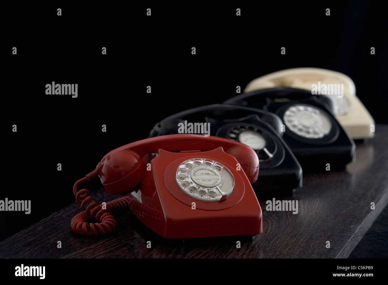 A row of old-fashioned dial telephones on a desk, a red one in the foreground Stock Photo