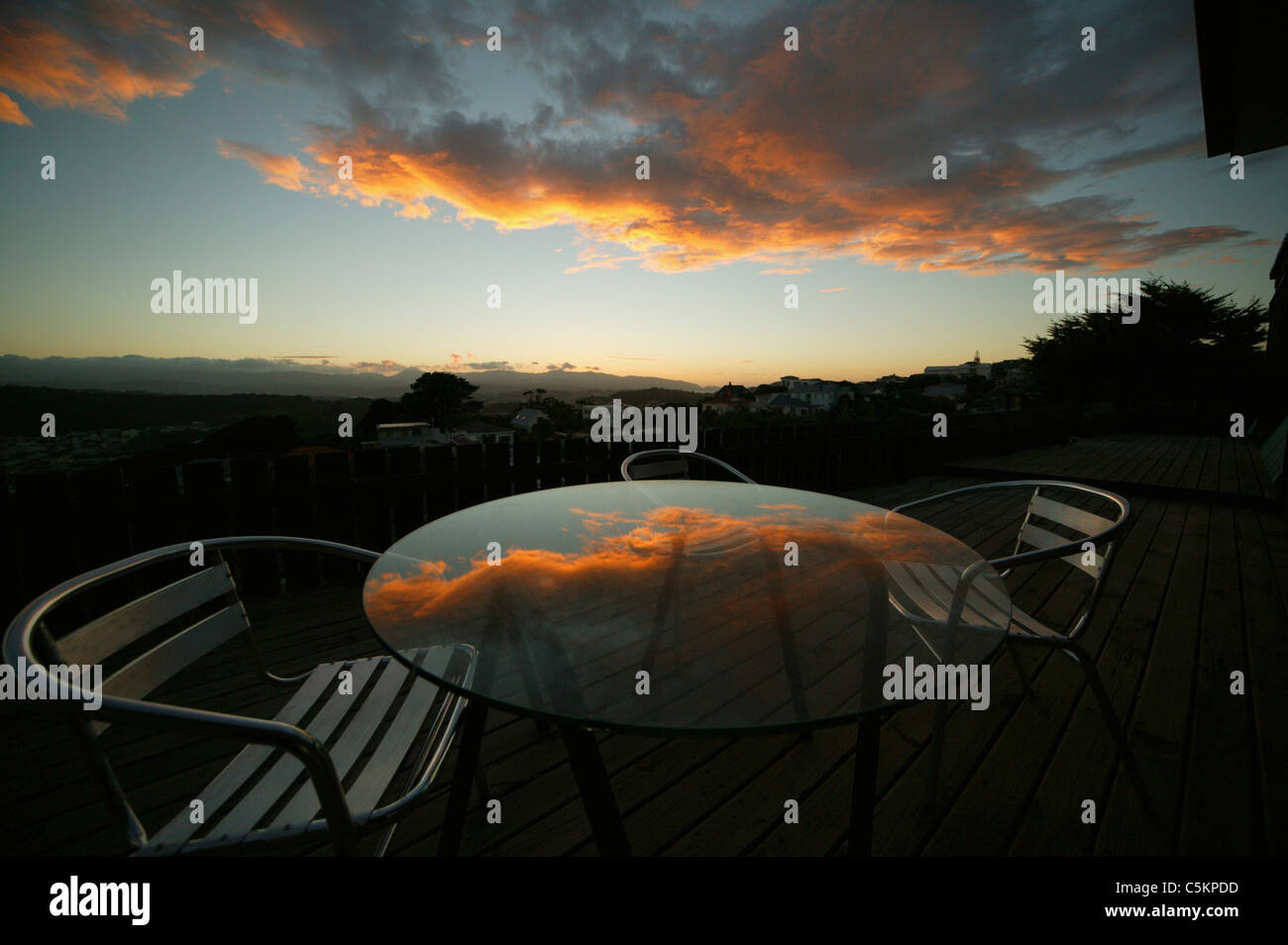 Sunrise reflected in round glass table on a deck with aluminum chairs, Wellington, New Zealand