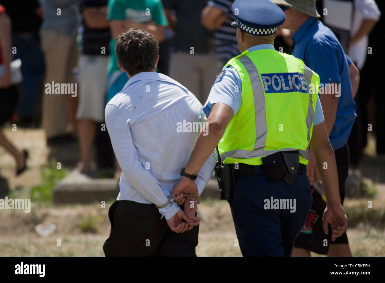 A young man, back view, being taken away in handcuffs by a policeman at Trentham Racecourse on Wellington Cup Day, Upper Hutt, Stock Photo