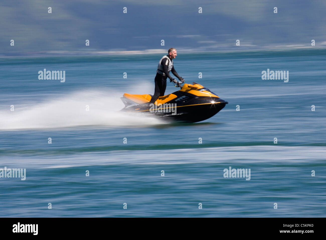 Man (30S) driving a jet-ski at speed while standing, wearing a wetsuit, with motion blur, Wellington, New Zealand Stock Photo