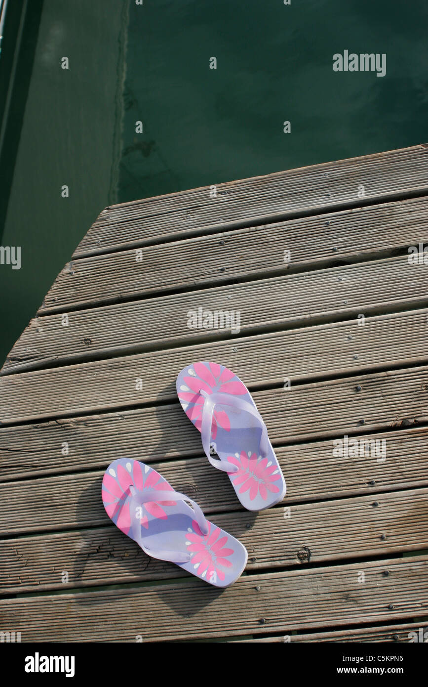 Pair of plastic sandals with floral pattern on wooden wharf over water ...