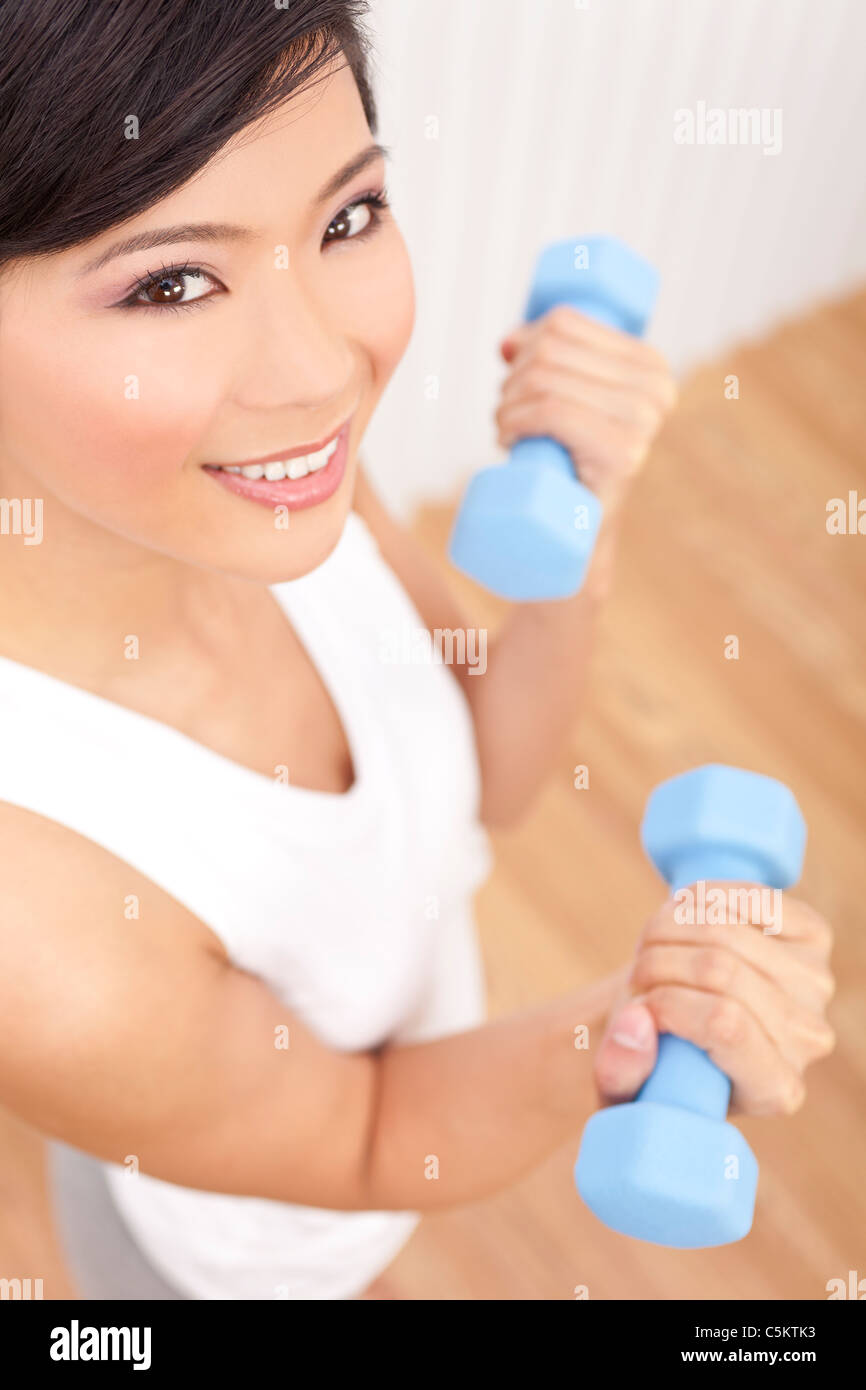 A beautiful young Chinese Asian Oriental woman lifting blue weights or dumb bells while exercising at a gym Stock Photo