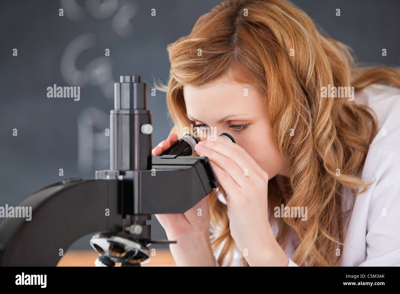 Blond-haired woman looking through a microscope Stock Photo