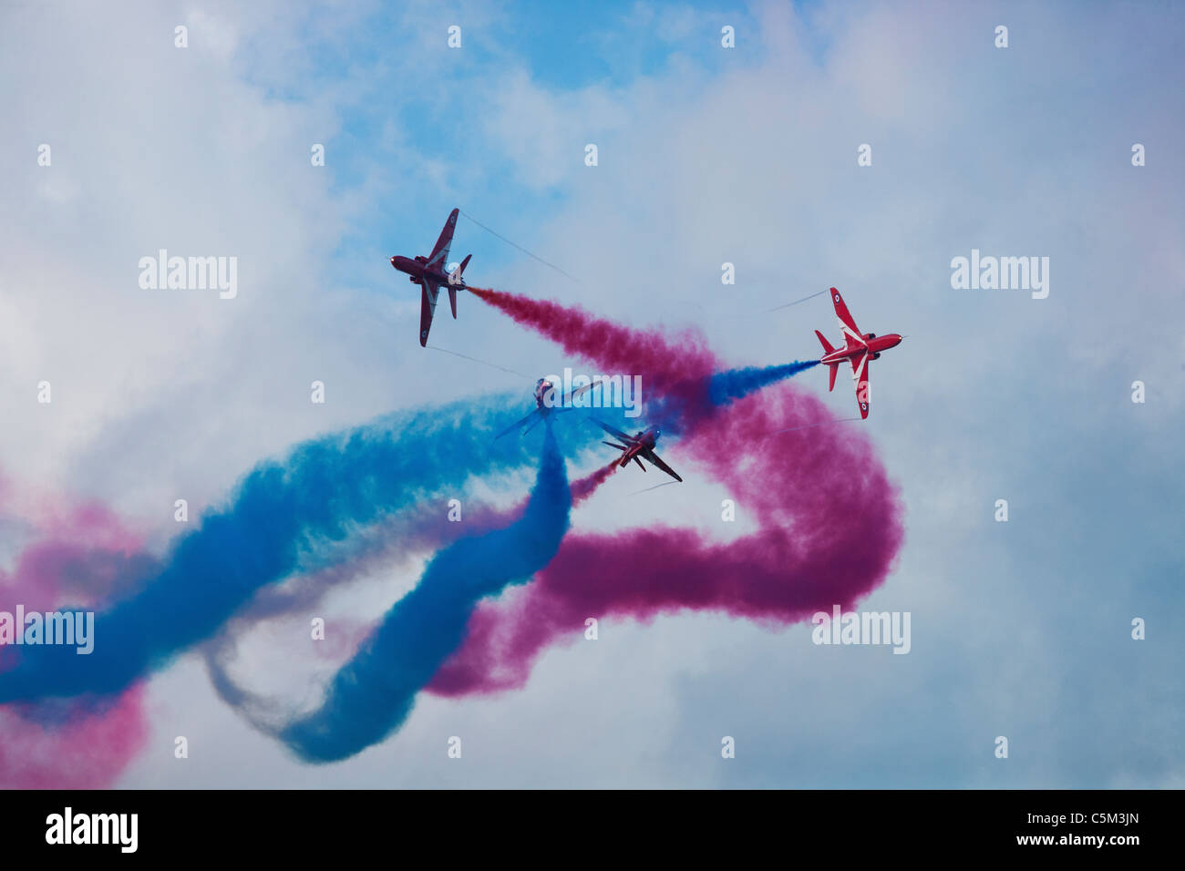 The Red Arrows performing a complicated maneuver with blue and red smoke behind Stock Photo