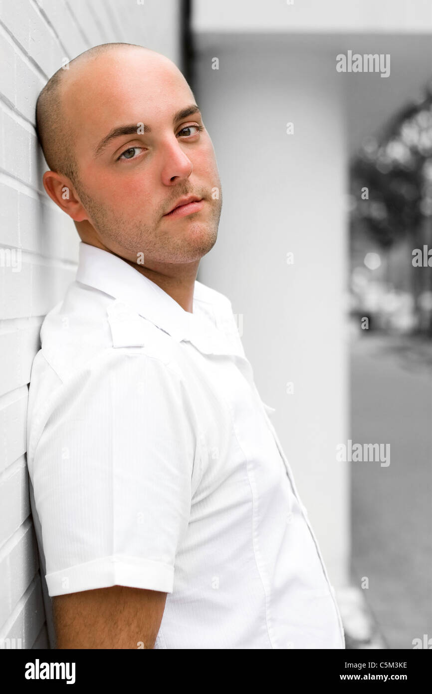 Portrait of a young man in the city leaning against a white brick wall ...