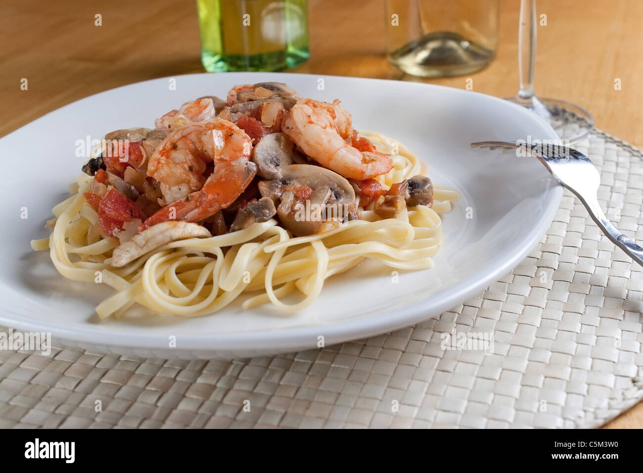 A delicious shrimp scampi pasta dish with mushrooms and diced tomatoes on a white plate. Stock Photo