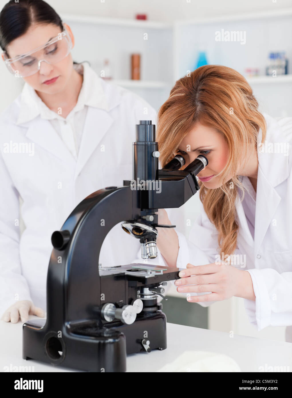 Blond scientist looking through a microscope with her assistant Stock Photo