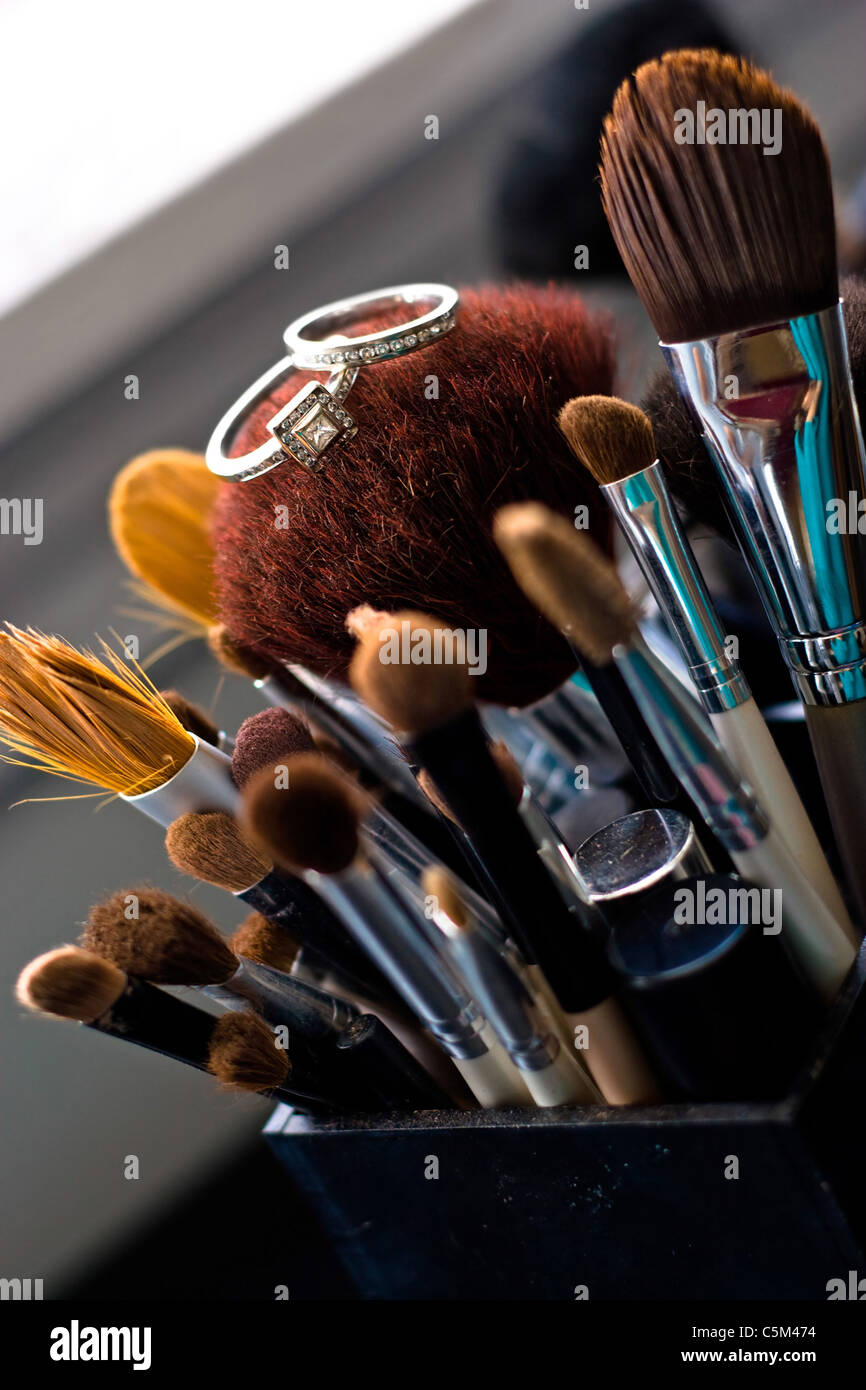 Two diamond wedding rings a band and engagement ring laying on top of some professional makeup brushes. Stock Photo