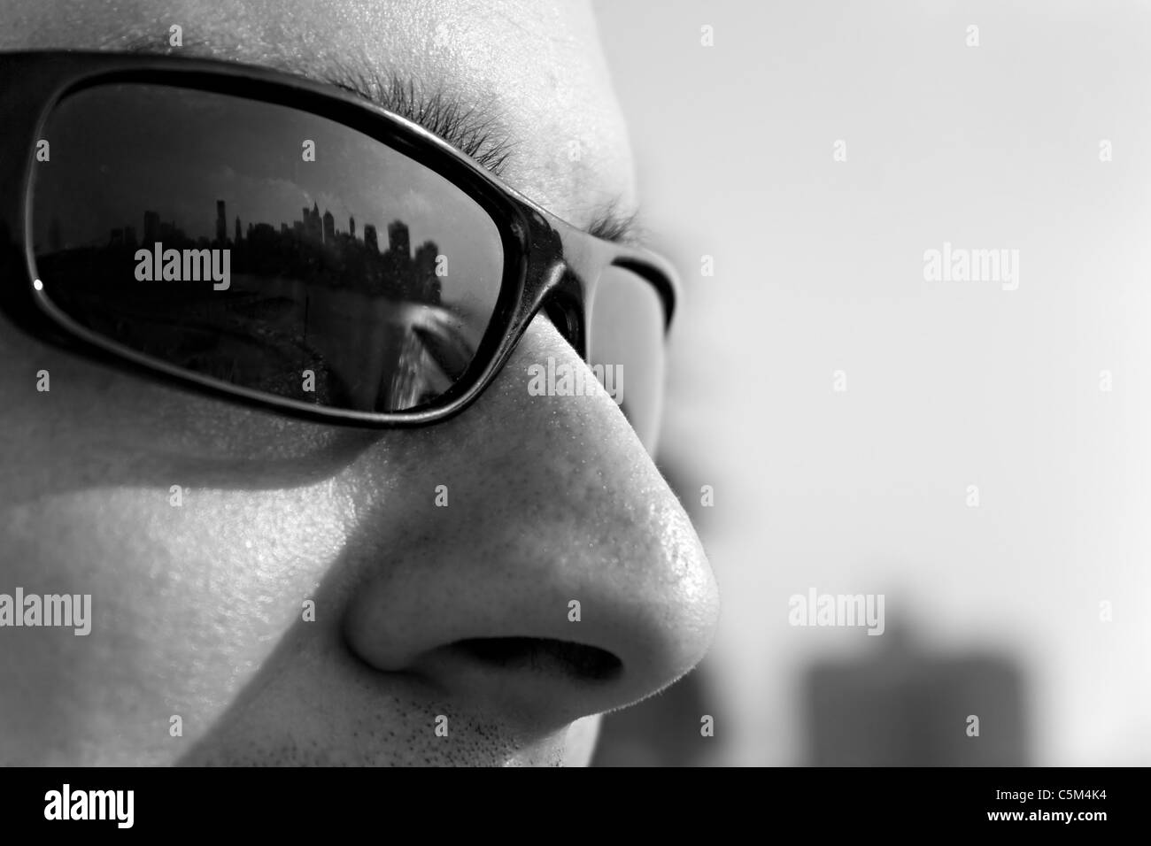 Close up of a man wearing sunglasses with the New York City skyline reflecting in the lens. Shallow depth of field. Stock Photo