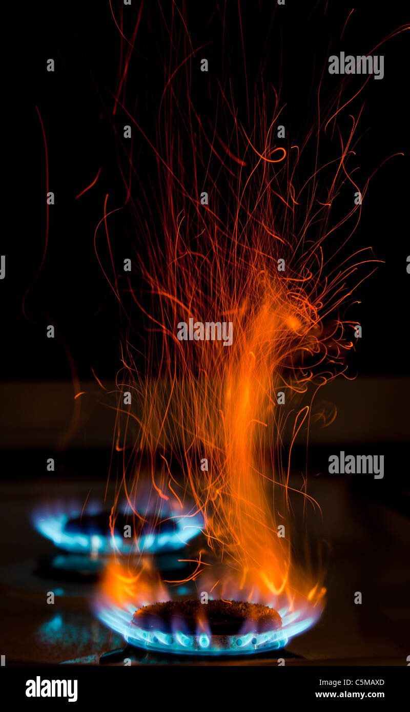 red and orange sparks and flames above gas stove burning with blue