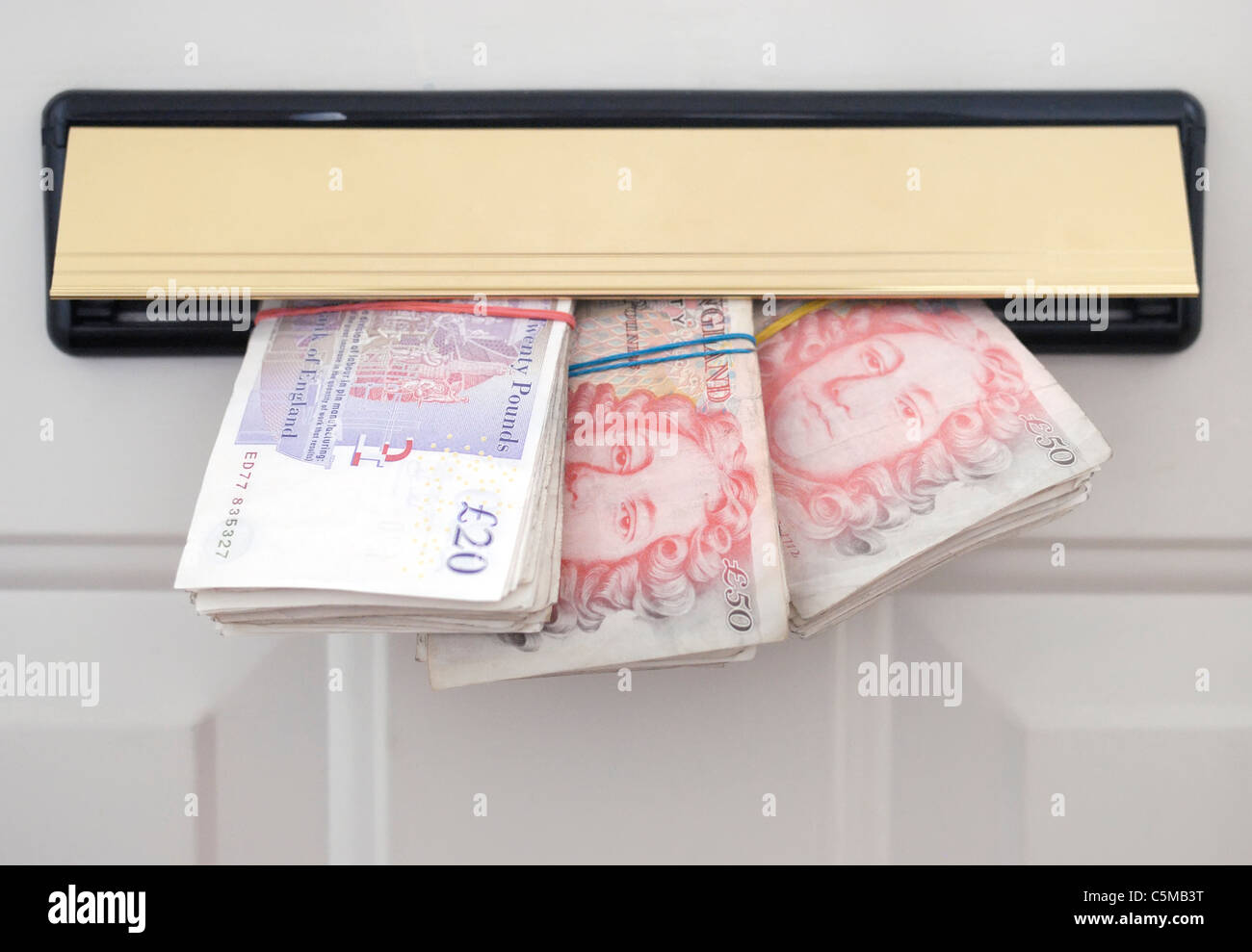 British banknotes poking through a letterbox in a door. Stock Photo