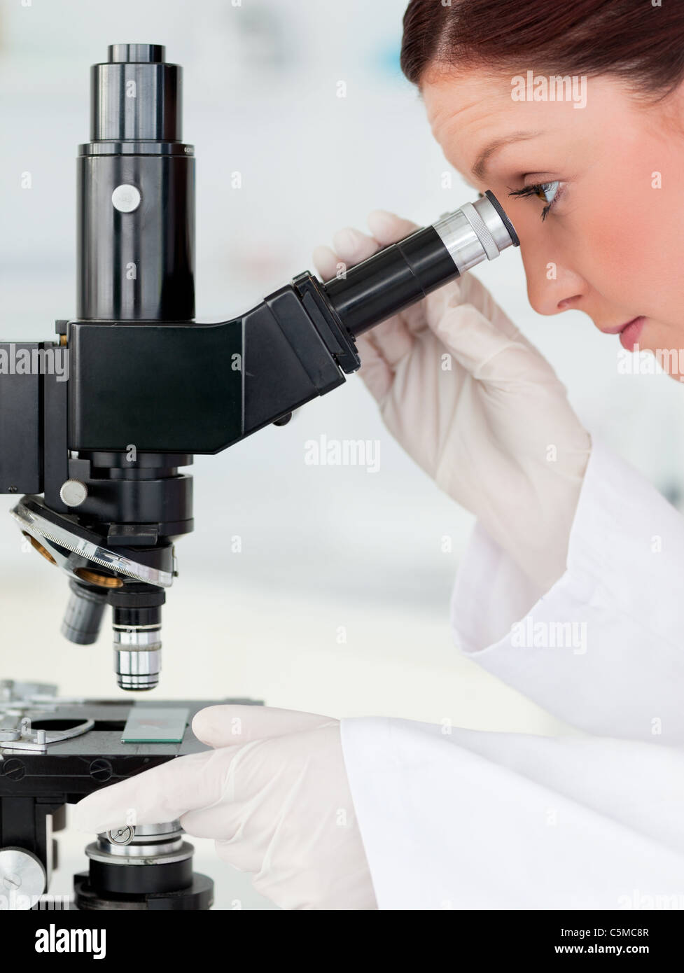 Good looking red-haired scientist looking through a microscope Stock Photo