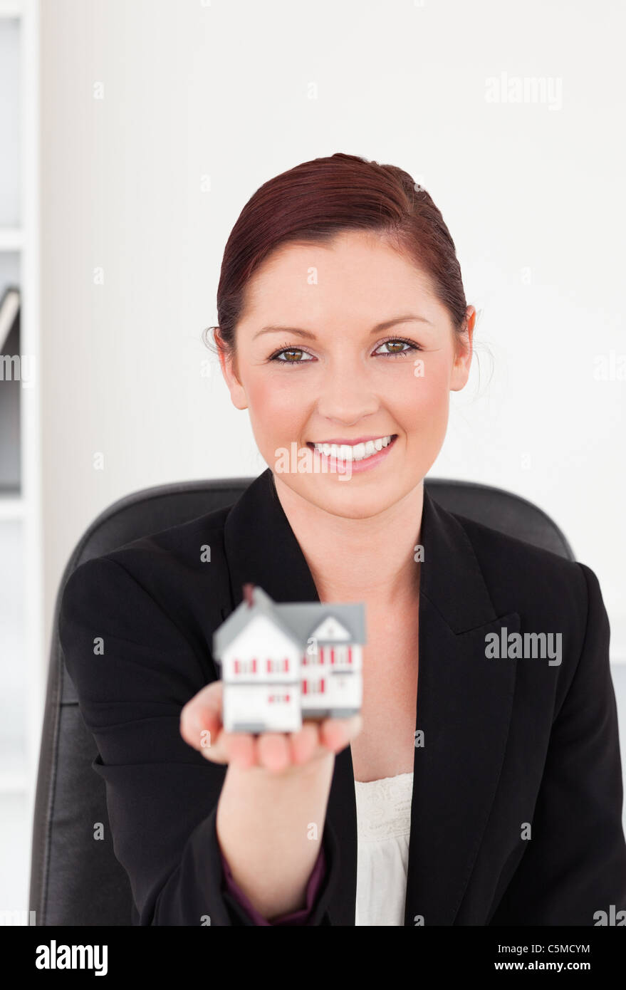Attractive red-haired woman in suit holding a miniature house Stock ...
