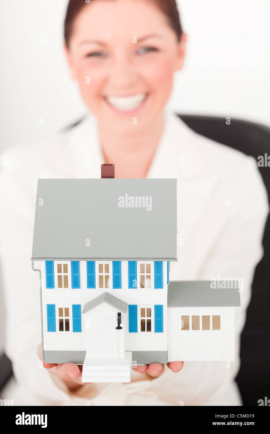 Young pretty red-haired female in suit holding a blue miniature house ...