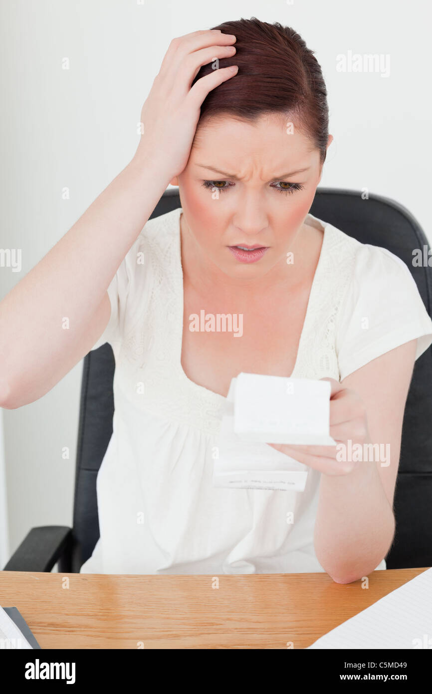 Young attractive red-haired female being stunned by the amount of the receipt Stock Photo