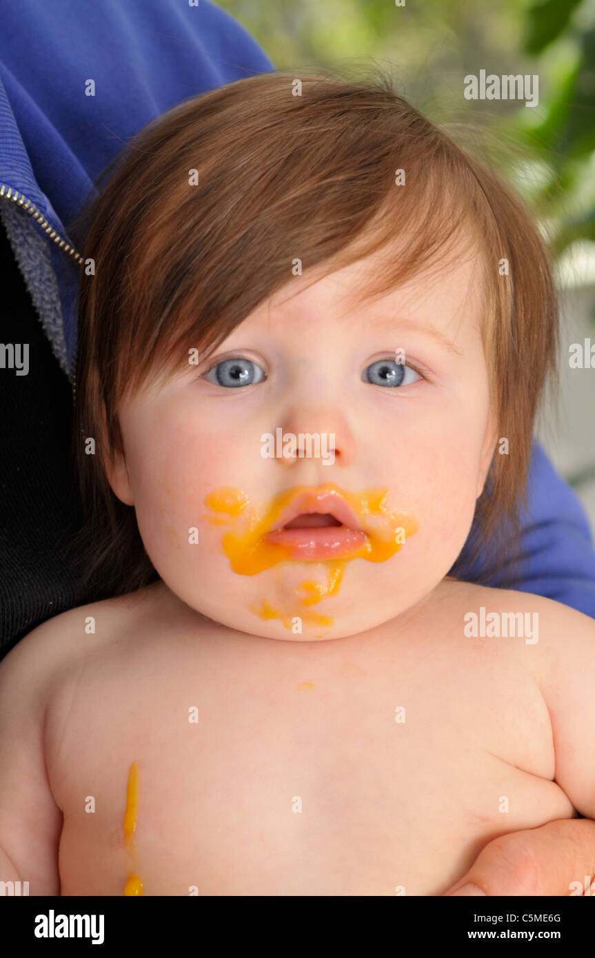 messy baby eating being held in her mothers arms. Stock Photo