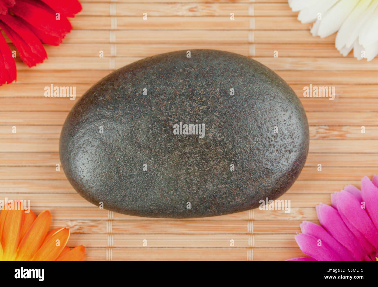 Round smooth pebble surrounded by colourfull gerberas Stock Photo