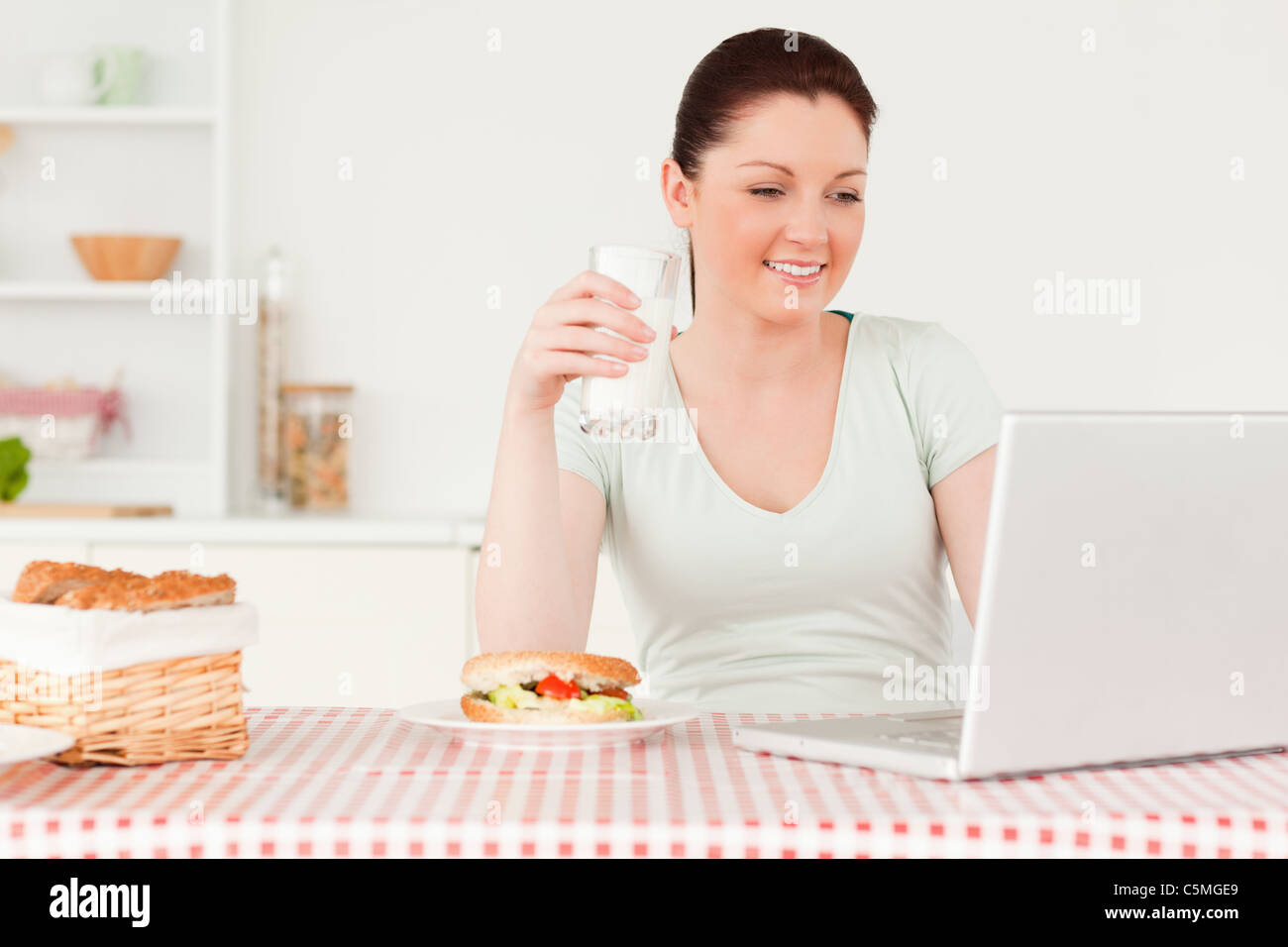 Smiling woman relaxing on her laptop while drinking a glass of milk Stock Photo