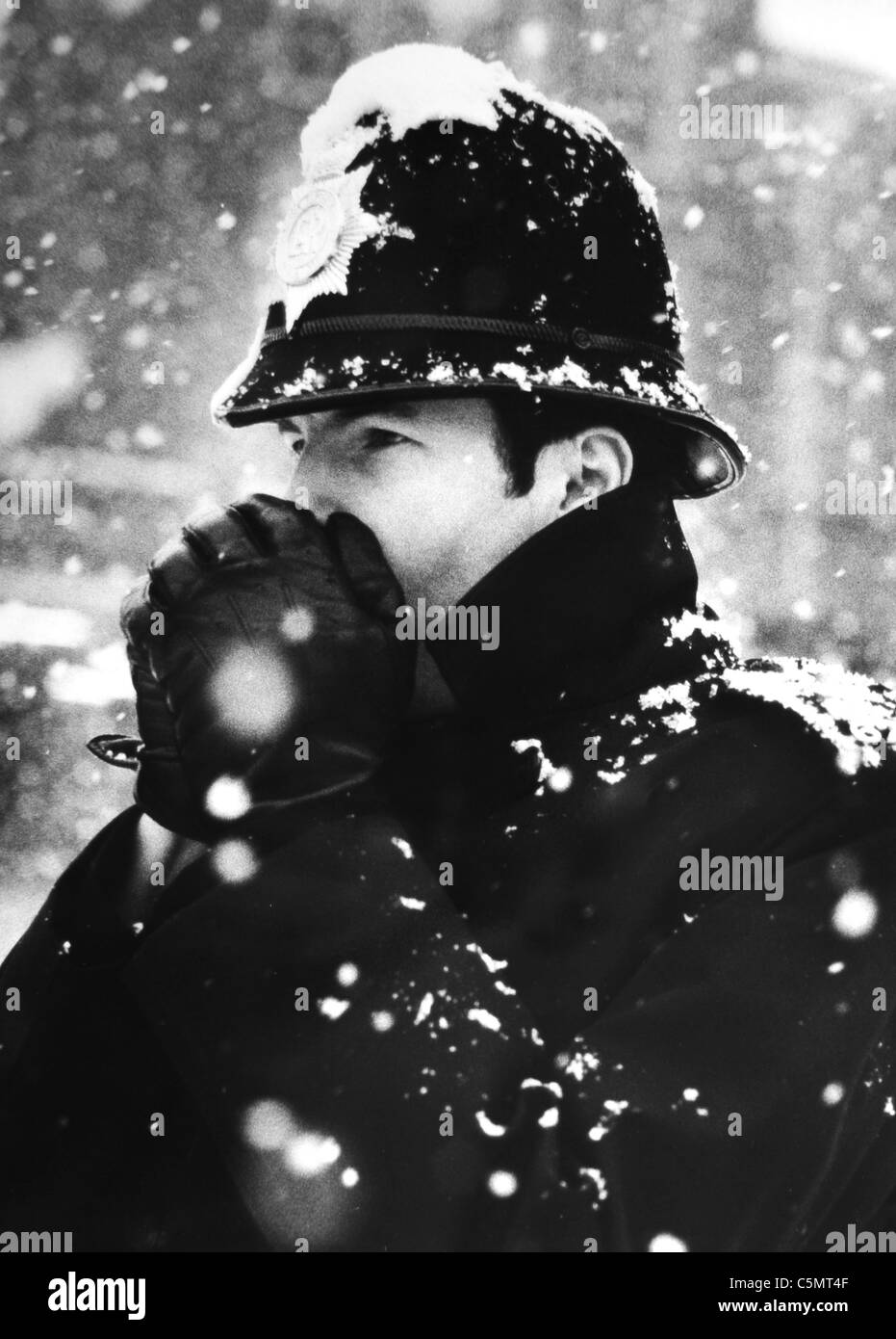A policeman on the beat in Crawley West Sussex blows his hands to keep warm during a snow storm in February 1983 Stock Photo