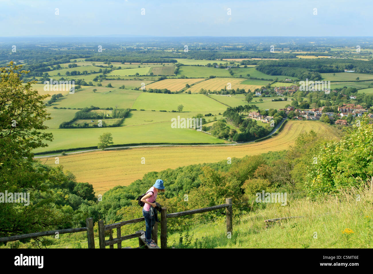 A woman climbs a stile at Devils Dyke near Brighton in the South Downs National Park; Sompting and the Weald in the background. Stock Photo