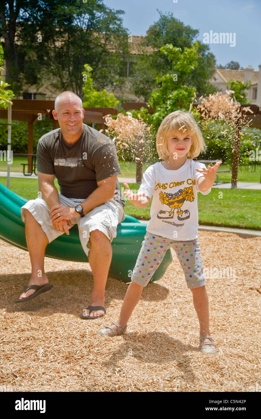 An affectionate father watches his daughter playfully throw wood chips