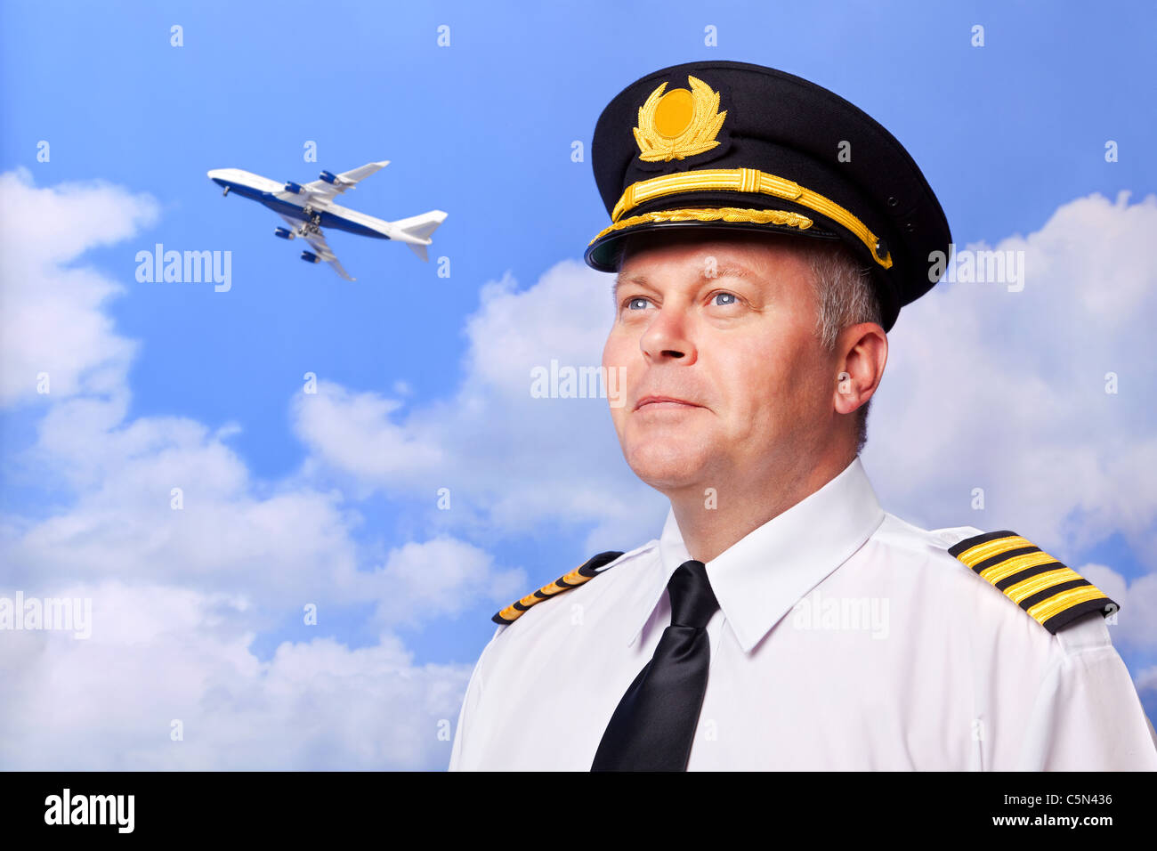 Photo of an airline pilot wearing the four bar Captains epaulettes, shot against a sky background with jumbo jet taking off Stock Photo