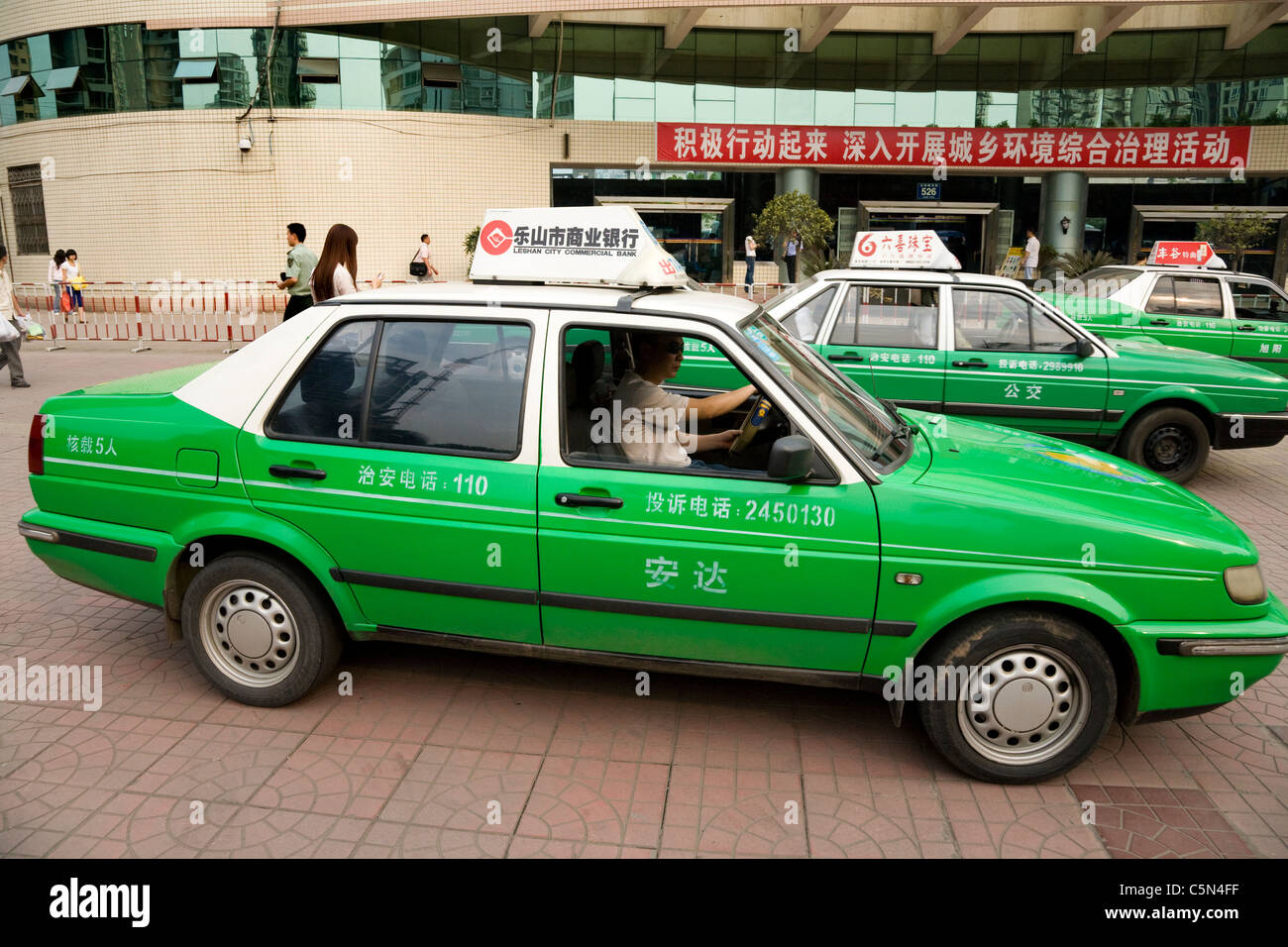 VW Taxi cab and driver wait for passengers / fare on a rank outside the bus station in Leshan city, Sichuan Province. China. Stock Photo