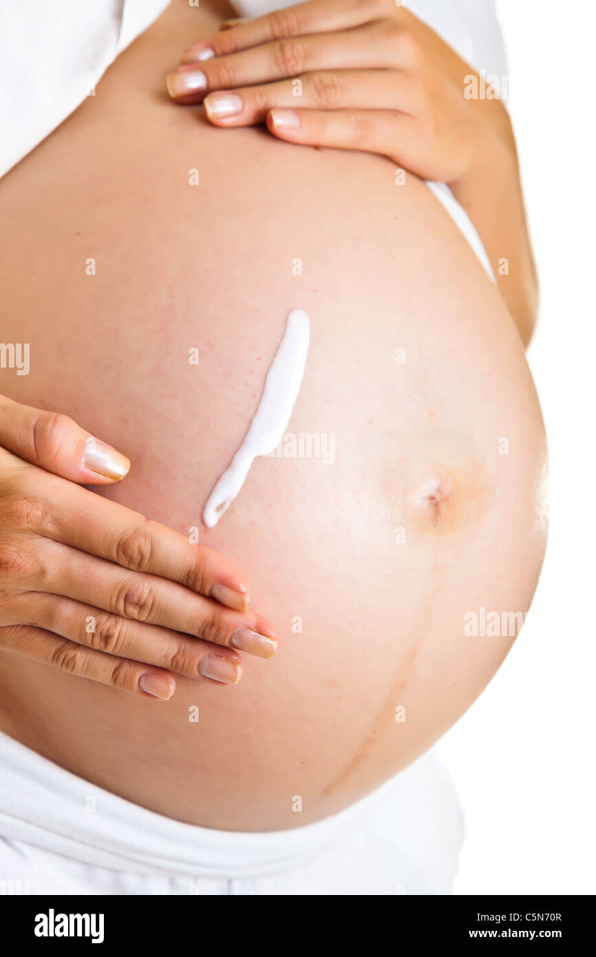 Pregnant woman moisturising belly to avoid stretch marks isolated on white Stock Photo