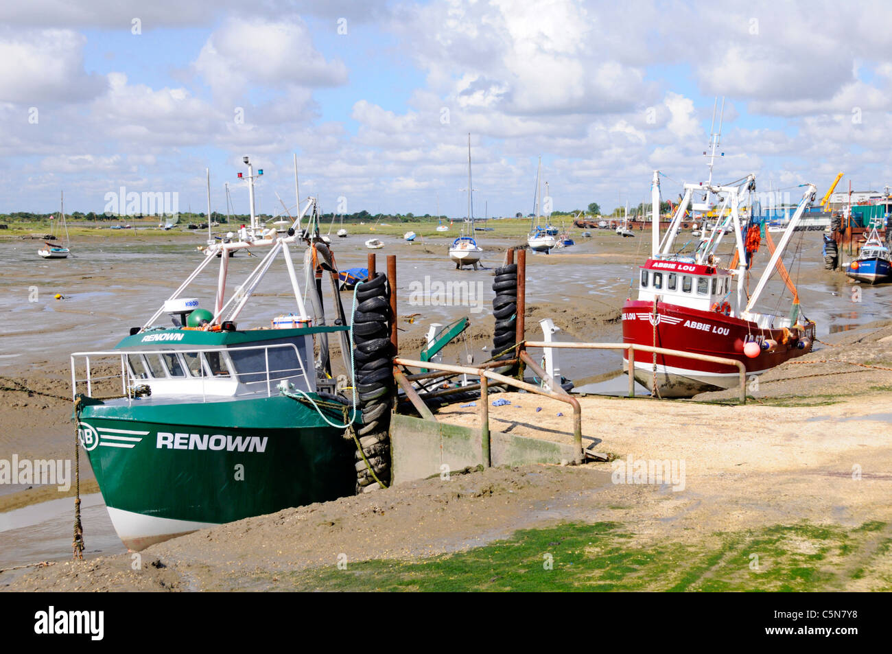 Cockle fishing boats moored Thames Estuary mud flats low tide creek beside unloading & handling facility for shellfish at Old Leigh on Essex coast UK Stock Photo