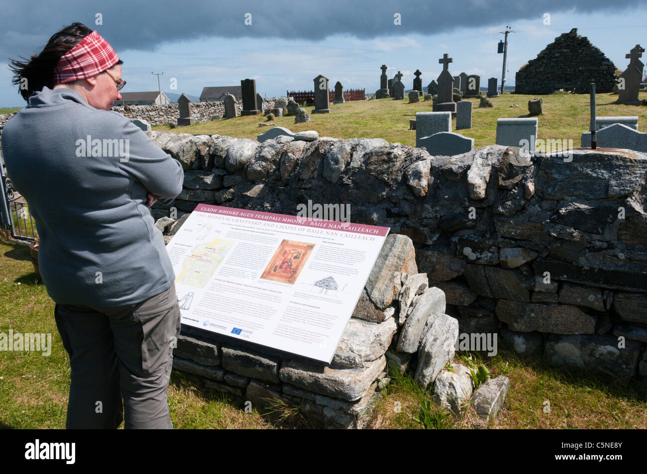 A tourist reads an interpretative sign at Cladh Mhuire chapel and graveyard on Benbecula in the Outer Hebrides Stock Photo
